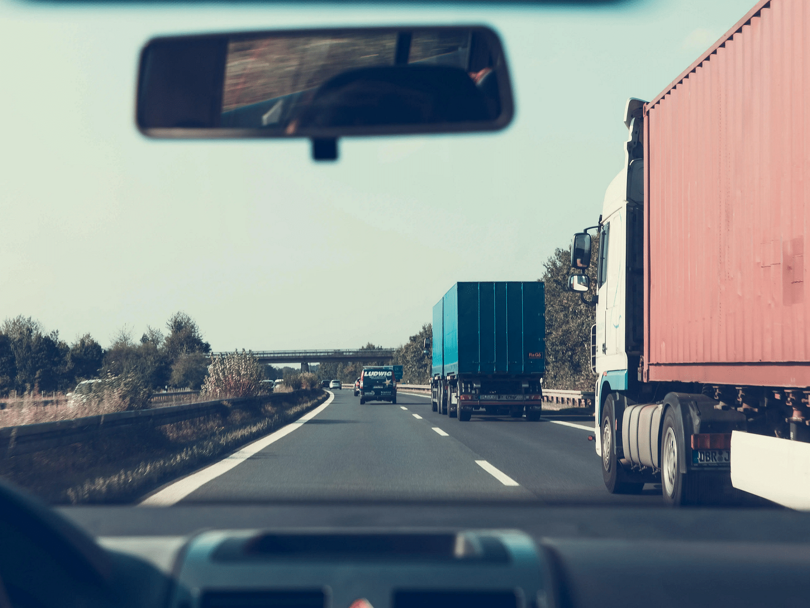 View from inside a moving car on a highway, passing container trucks under a clear sky.