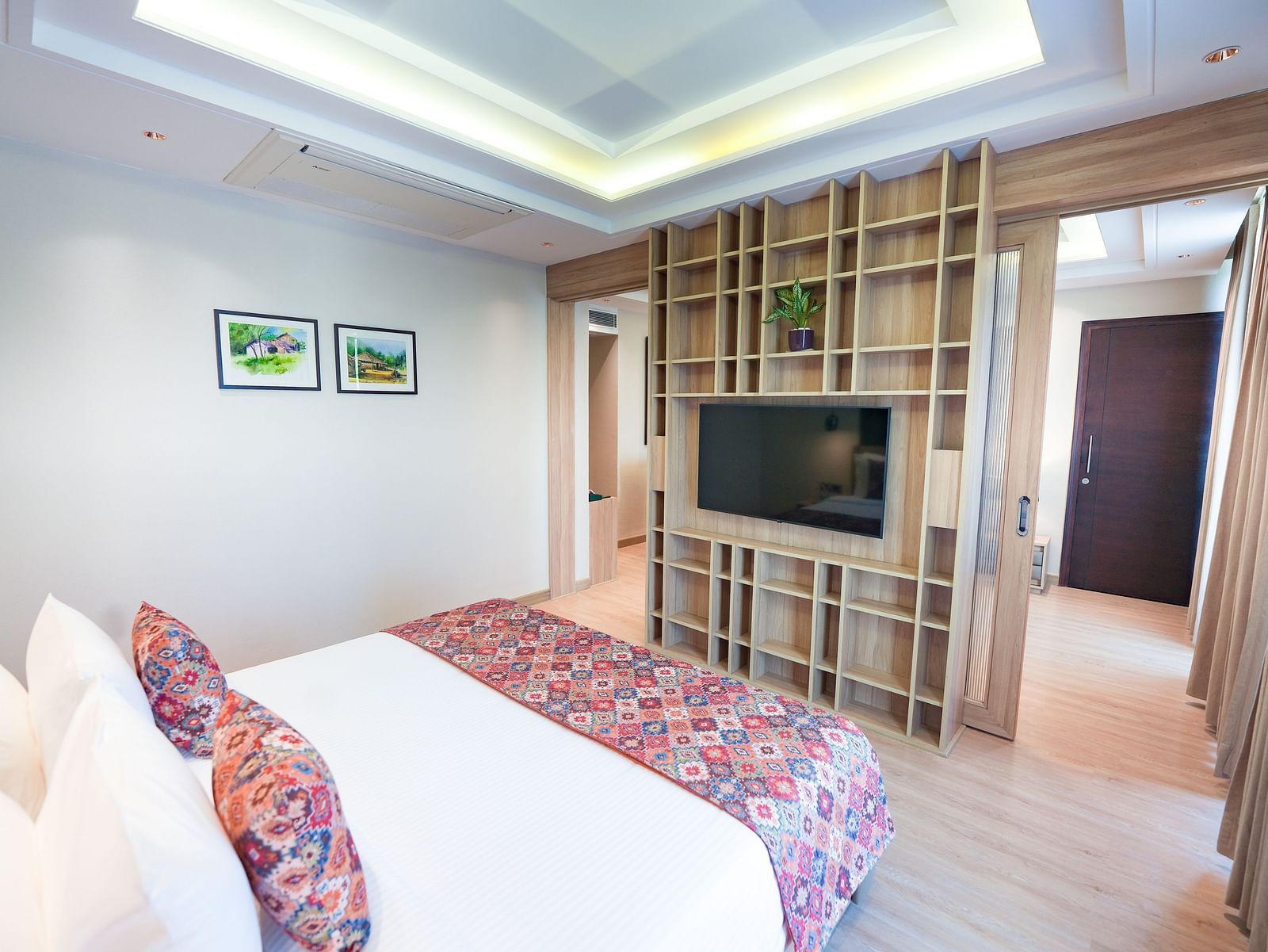 A bed in our suite featuring a floral-patterned bed runner and pillows, positioned in front of a wall-mounted television - NAMAMI BY ZENQ BANKHANDI