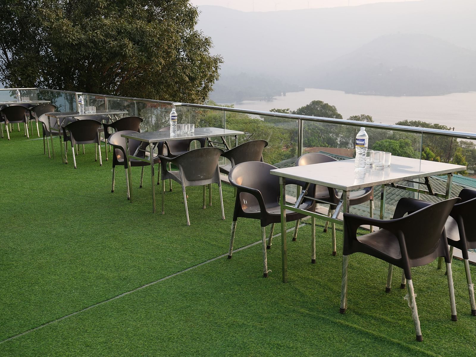 An image of the Lake View Oasis restaurant with chairs and tables at the rooftop and mountains and lake view in the background - Nisarga Lake Resort