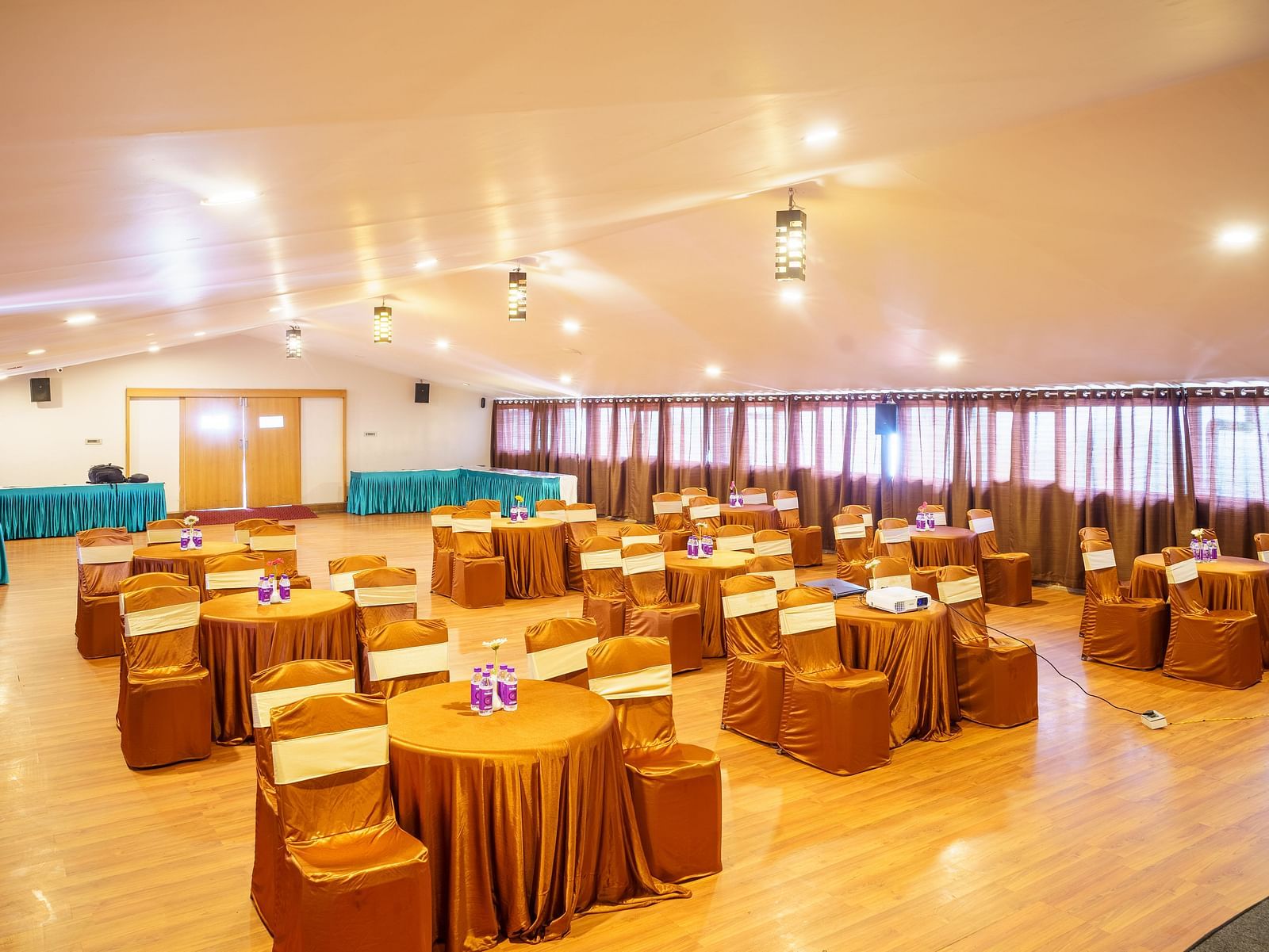 A large event hall at Orsino Spa Resort with rows of chairs and tables, a stage with a screen, and a decorative ceiling with lights.