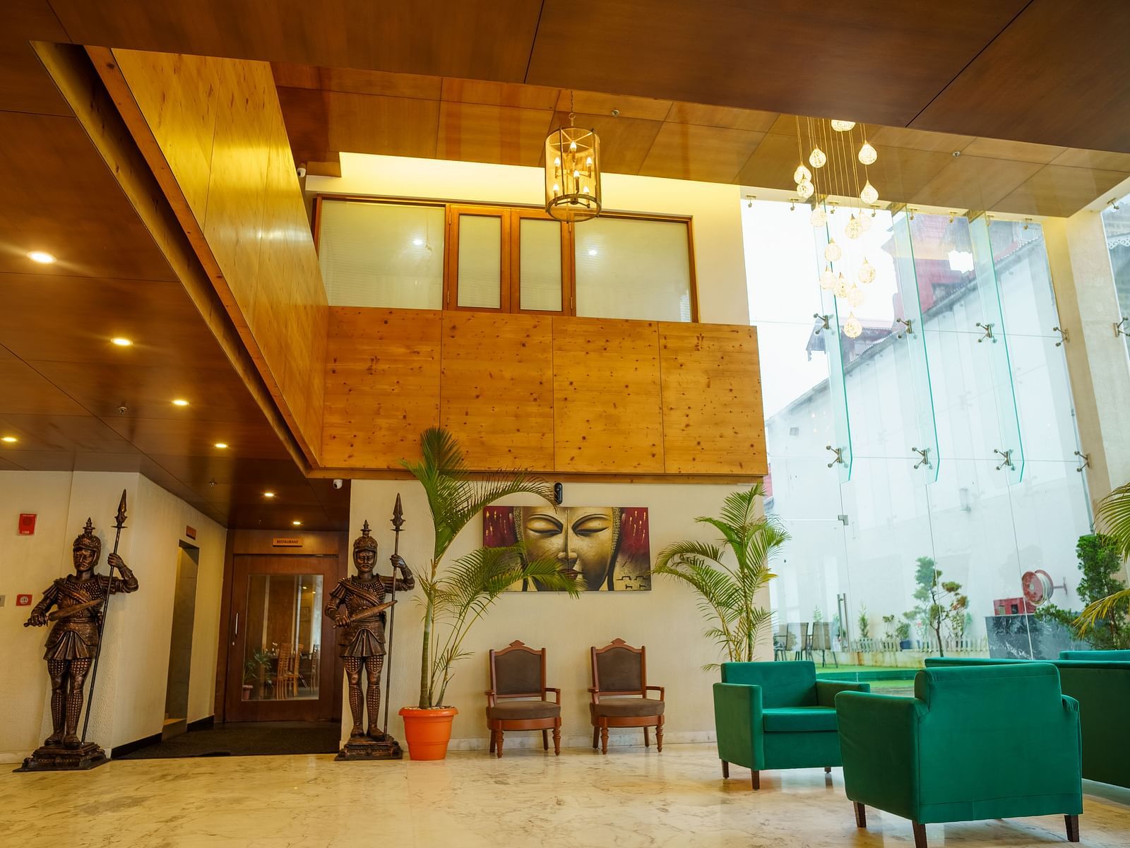 A view of an interior with green lounge furniture, a large statue, and natural light coming through tall windows at Orsino Spa Resort.