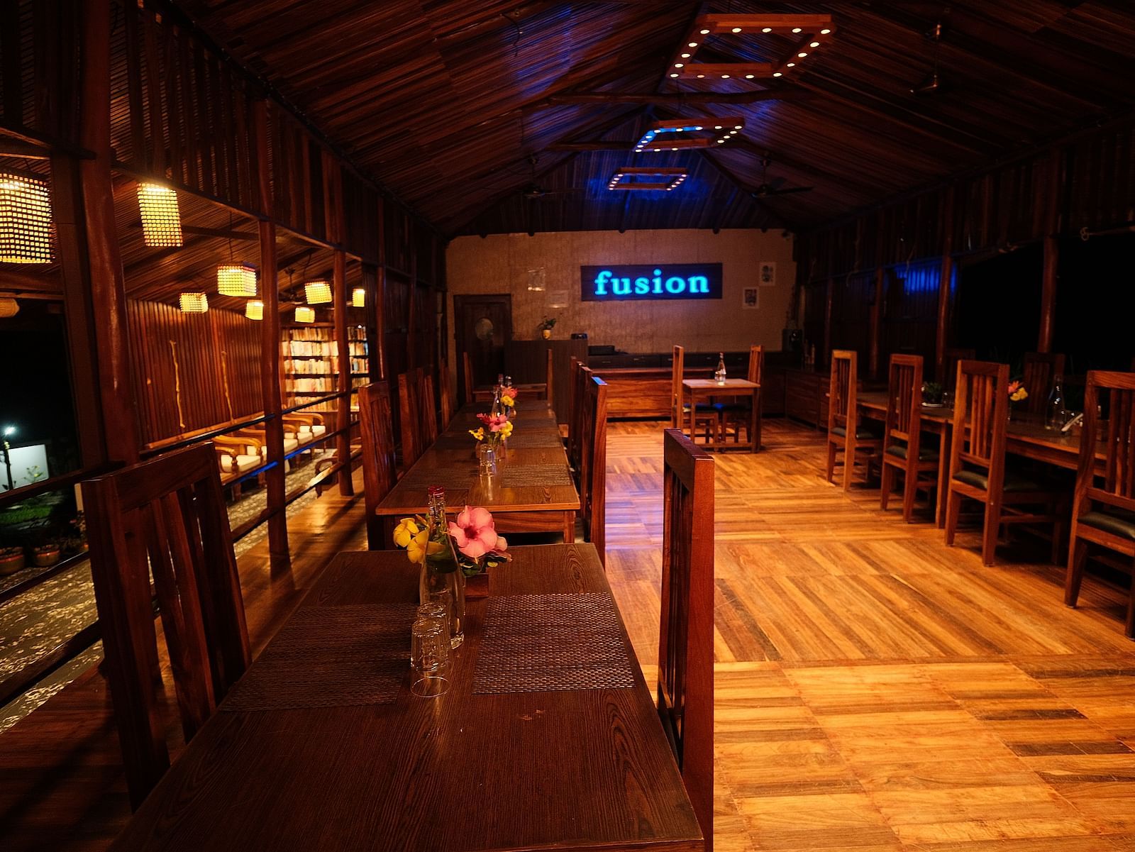 A wooden interior is illuminated by hanging lamps, highlighting the seating and shelving arrangements | Fusion Cafe and Multi-cuisine | RainForest Resort, Port Blair, Andaman and Nicobar Island