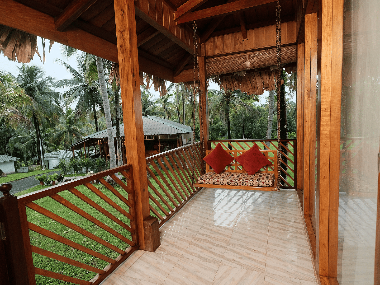 A close-up of a rustic wooden gazebo or porch with a thatched roof, featuring red cushions on a swing seat.