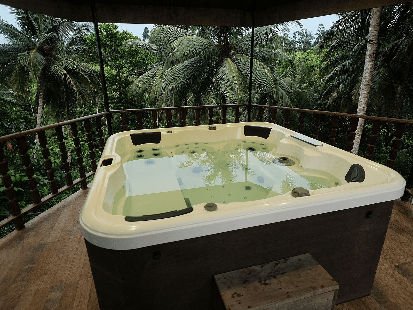 An outdoor jacuzzi on a wooden deck, surrounded by lush green palm trees and tropical foliage.