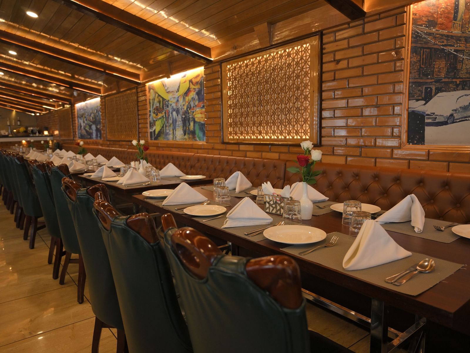 Tables and chairs arranged neatly with cutlery and decor ready for guests, with paintings on walls at Royal Comfort Regency