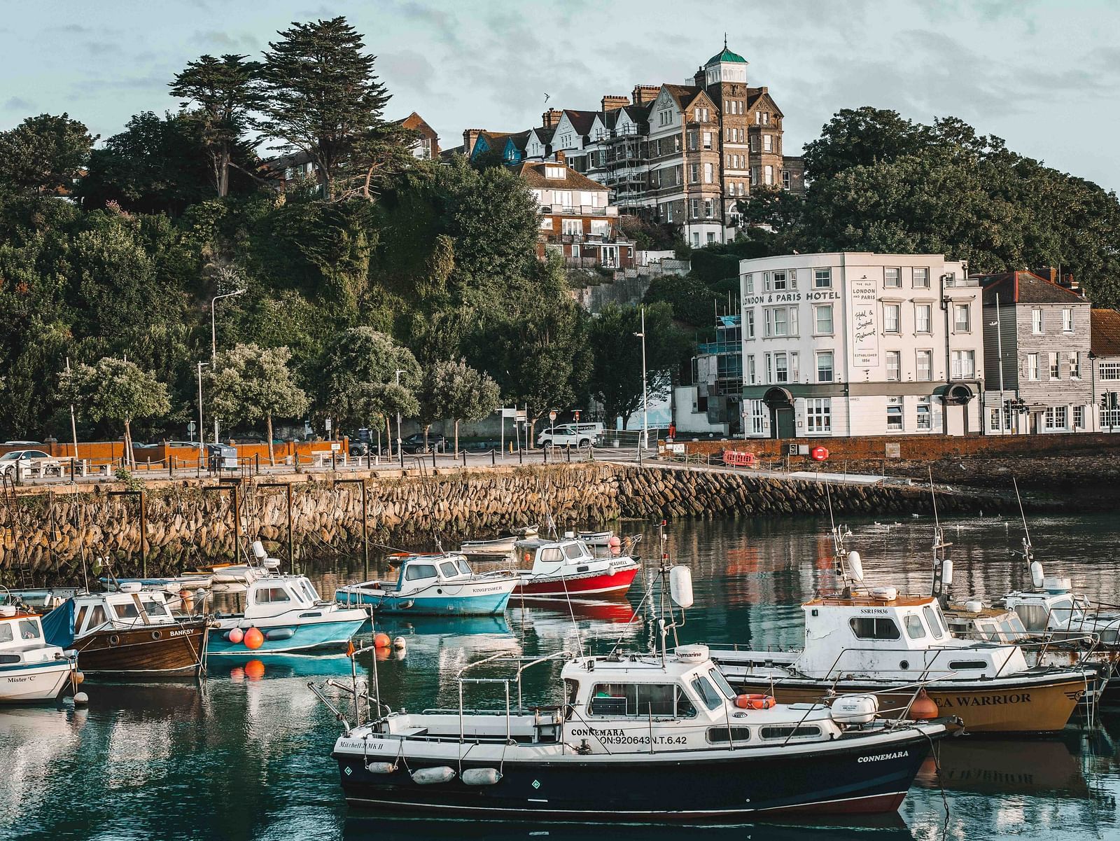 An overview of a marina with many boats parked on the waterbody and building in the background.
