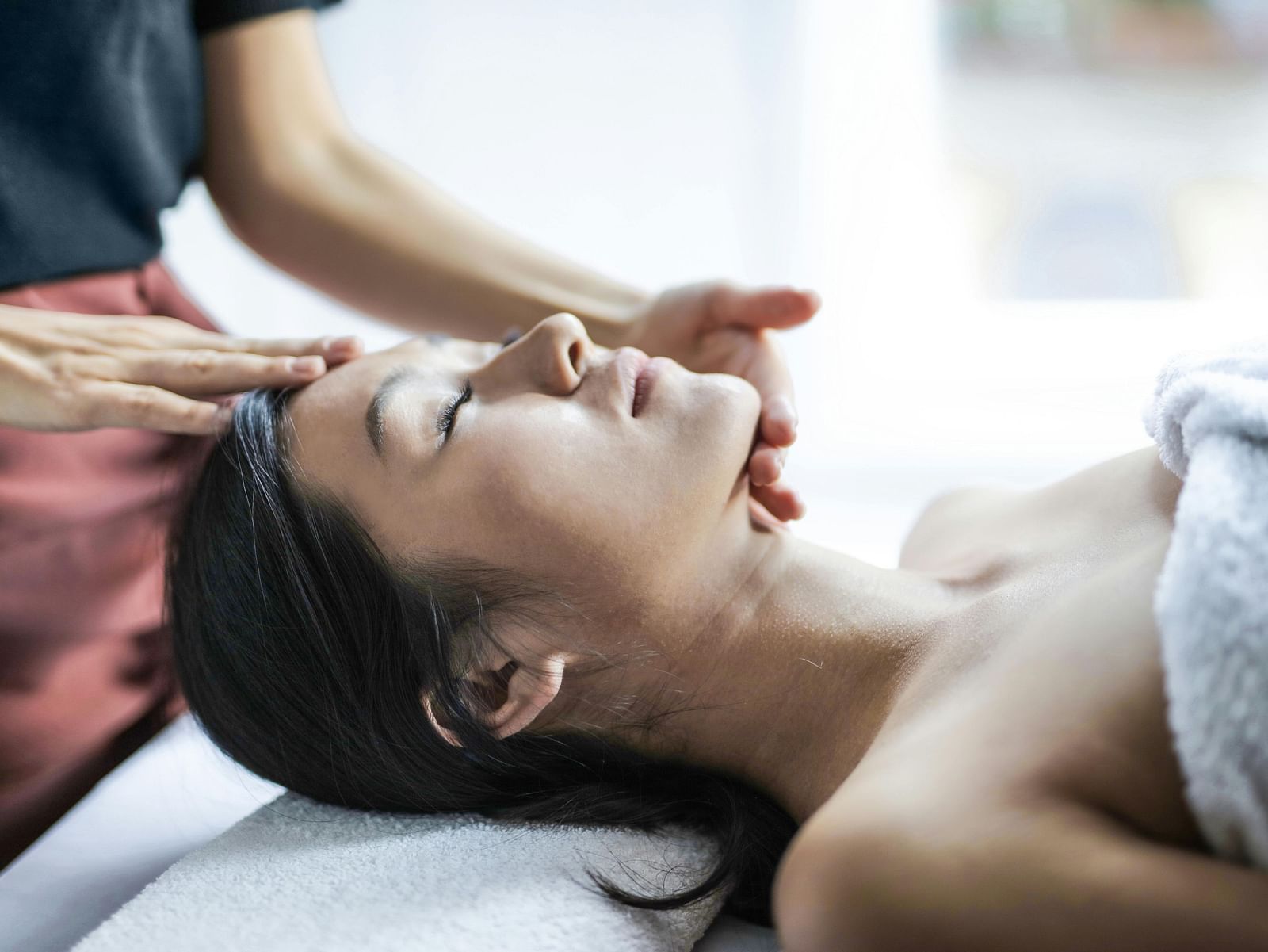  A person lies on a massage table receiving a facial or head massage.