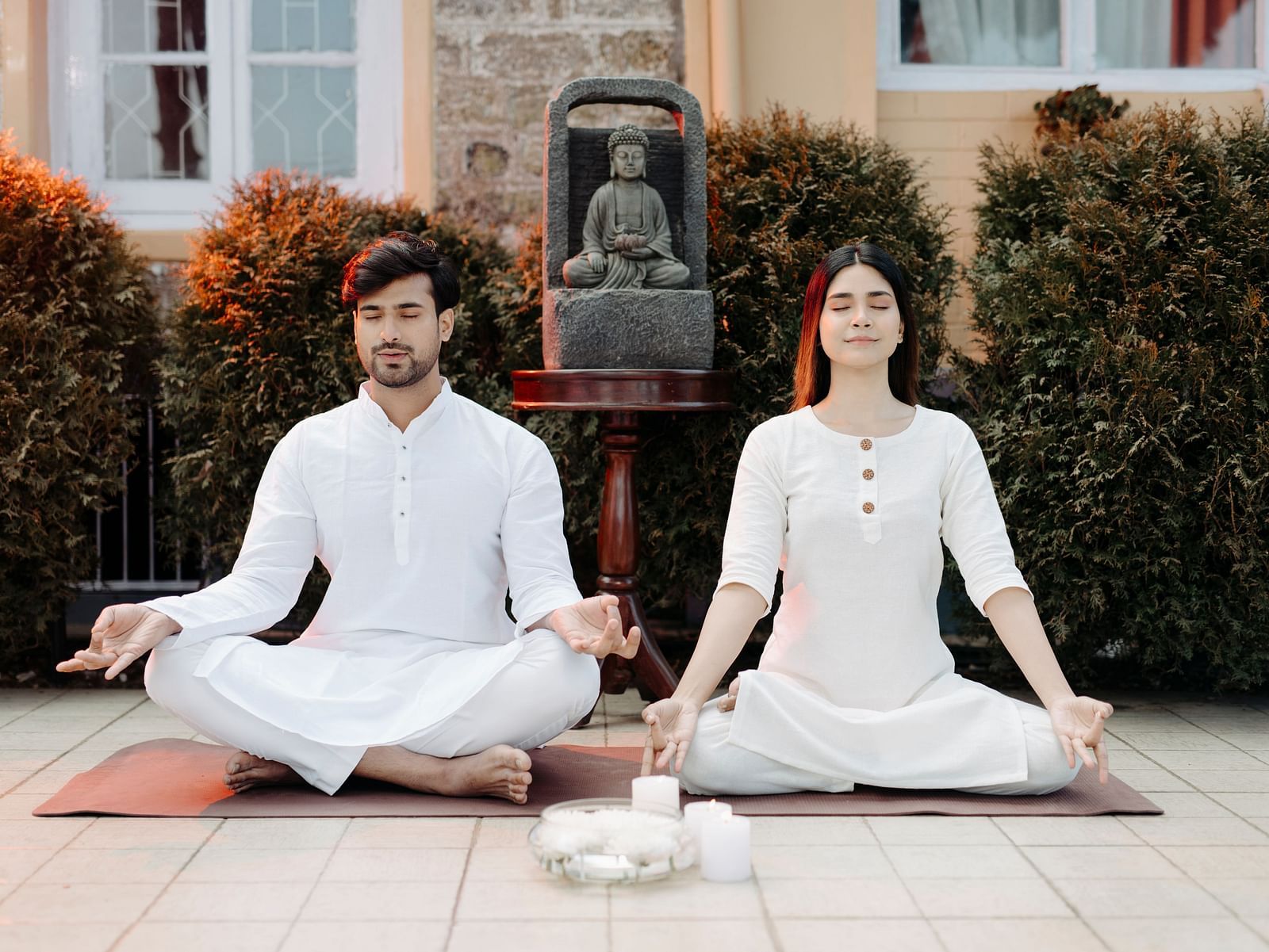 Man and woman meditating together in a serene outdoor space, dressed in white attire symbolizing tranquility.