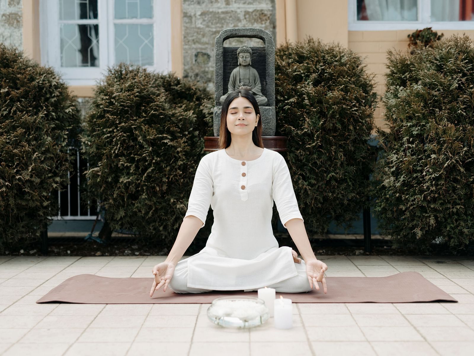 Woman practicing seated meditation outdoors on a yoga mat in a peaceful garden setting