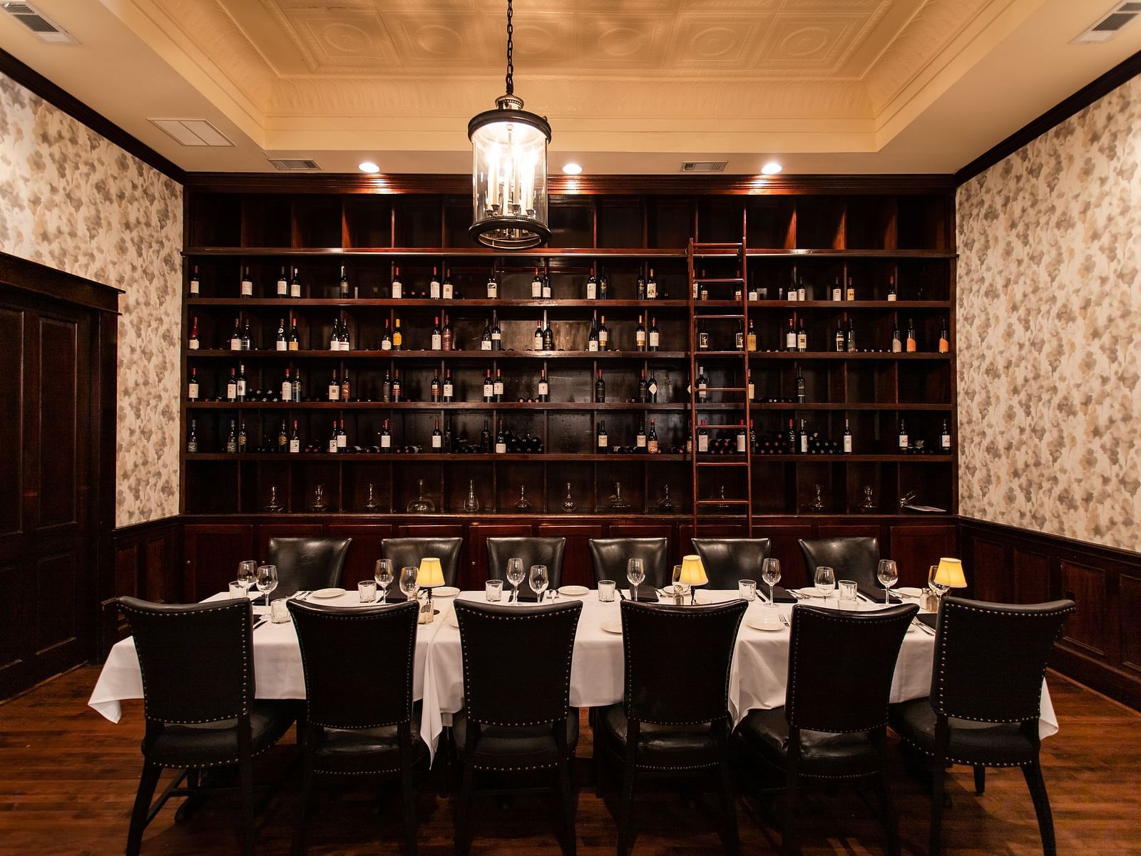 A  dining room with a long table, chairs, and a floor-to-ceiling rack of bottles against the back wall.- The Grand Hotel & Ballroom, McKinney