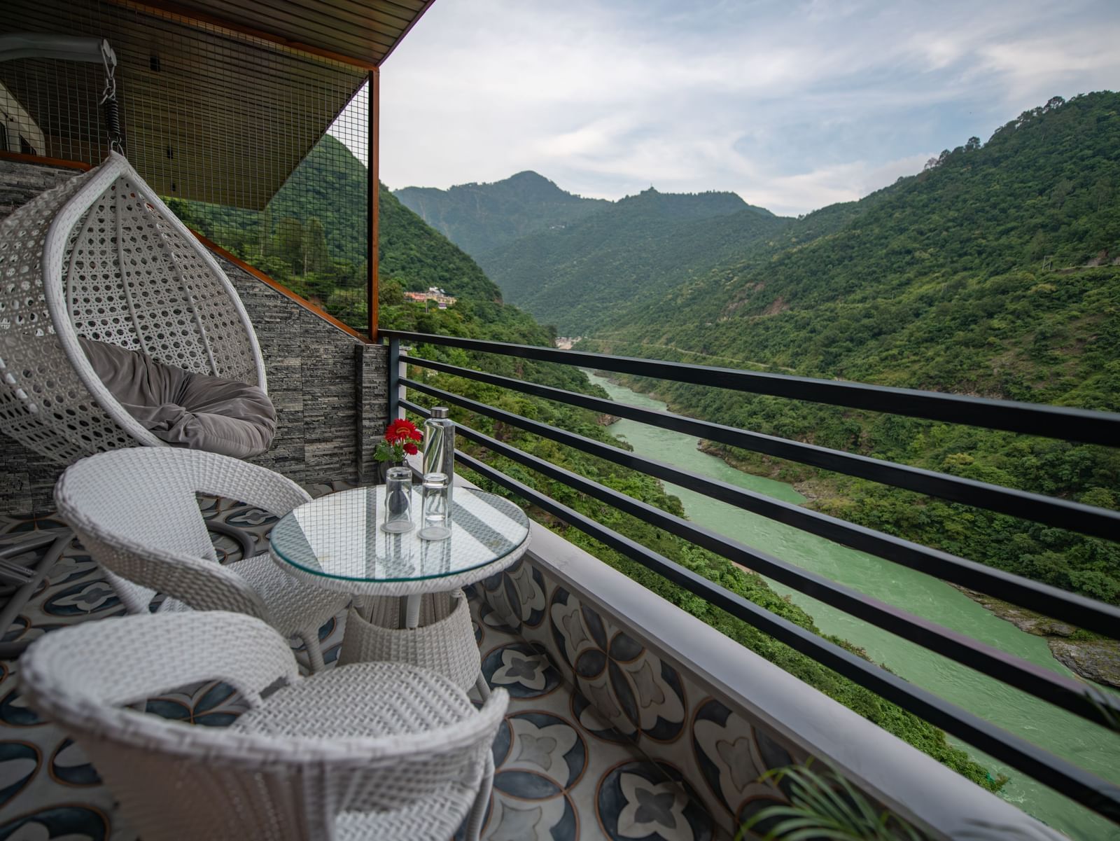 A balcony of a superior room at The Tattva Devaprayag offering a view of the expansive mountains and river. 