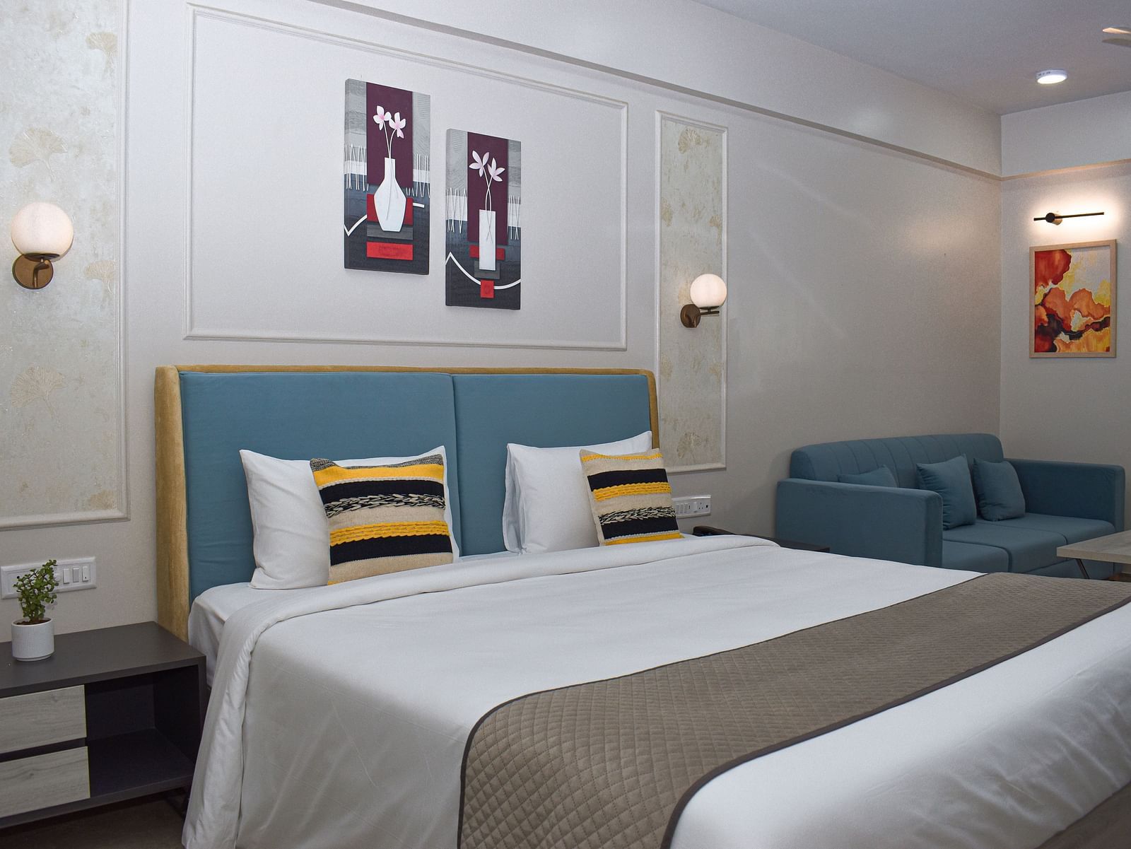 A Budget Hotel in Jaipur's room with a bed, a blue sofa, a small table, wall-mounted light fixtures, and framed artworks - Urban Suites by BluSalzz, Jaipur