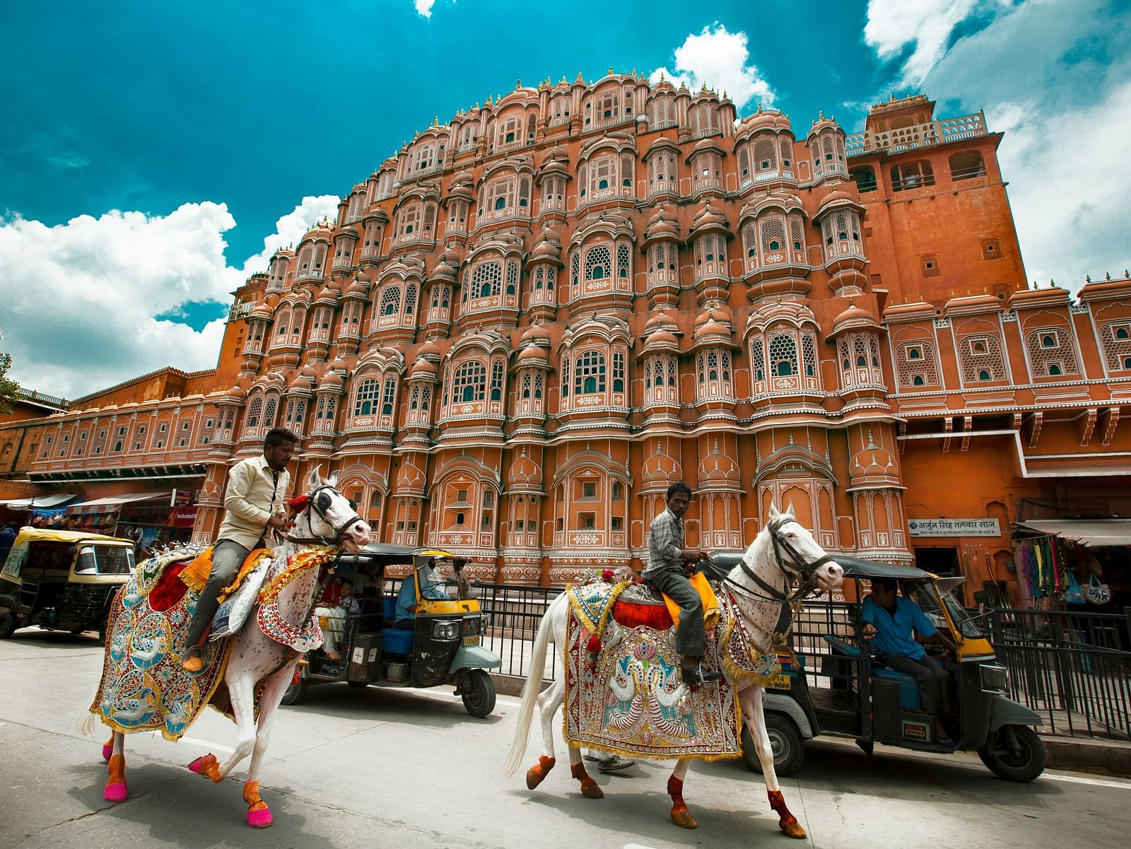 Hawa Mahal, Jaipur, with its distinctive pink facade and numerous windows, with two decorated horses in the foreground.