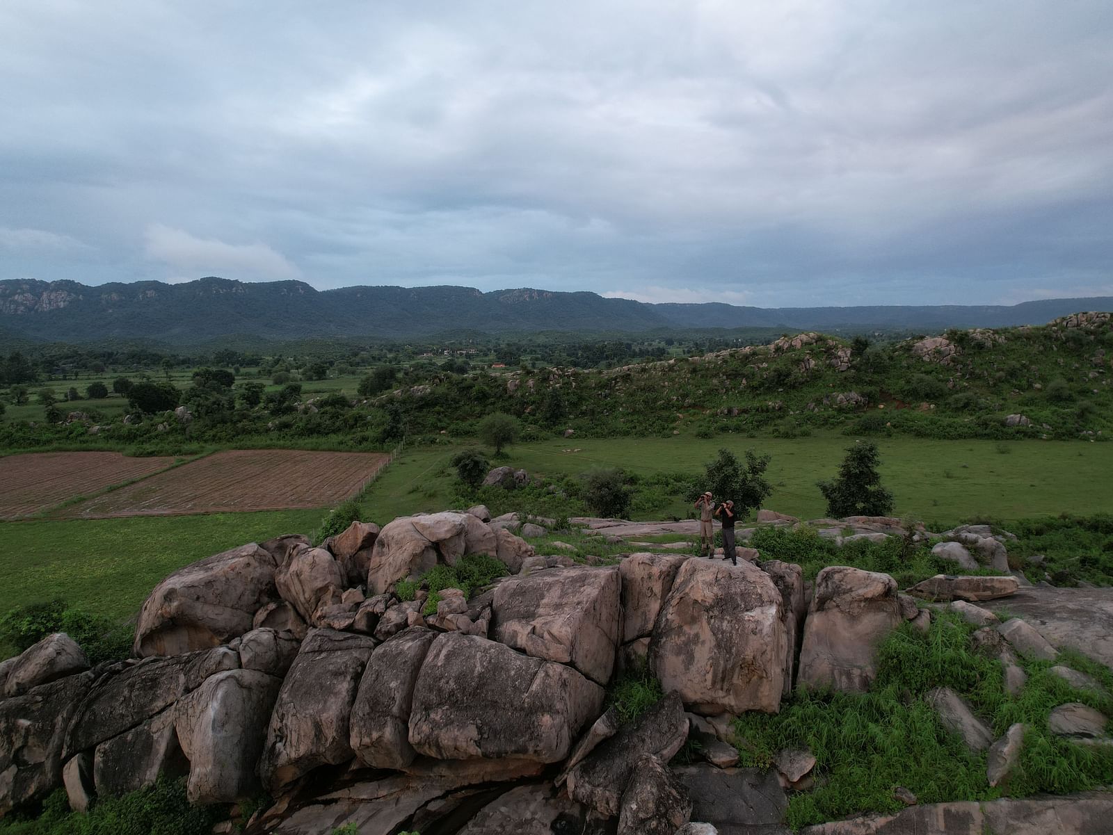 Two People standing on a rocky outcrop, holding binoculars.