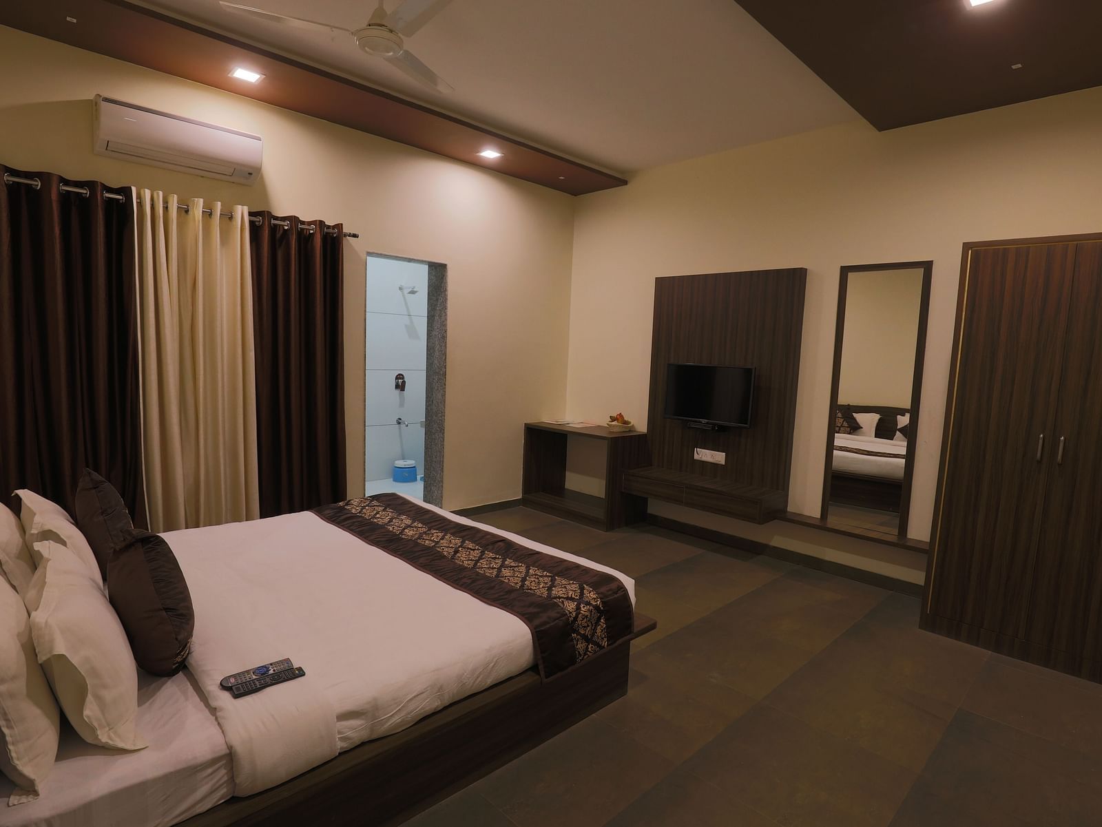 A comfortable bedroom with a double bed, dark furniture, and soft lighting - Vishal Lords Inn Gir Forest