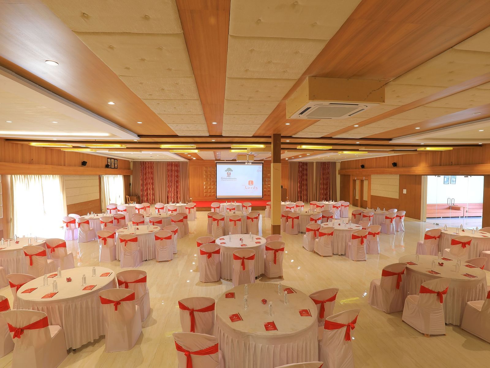 An expansive banquet hall with round tables draped in white and pink table cloth, ready for an event - Vishal Lords Inn Gir Forest