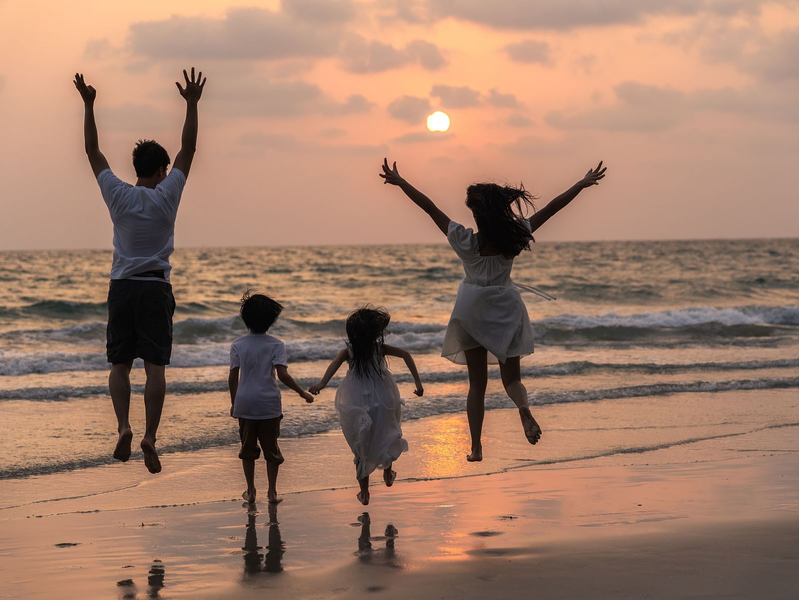 Family enjoying a beach vacation at sunset, with mom, dad, and child running and relaxing together near the sea.