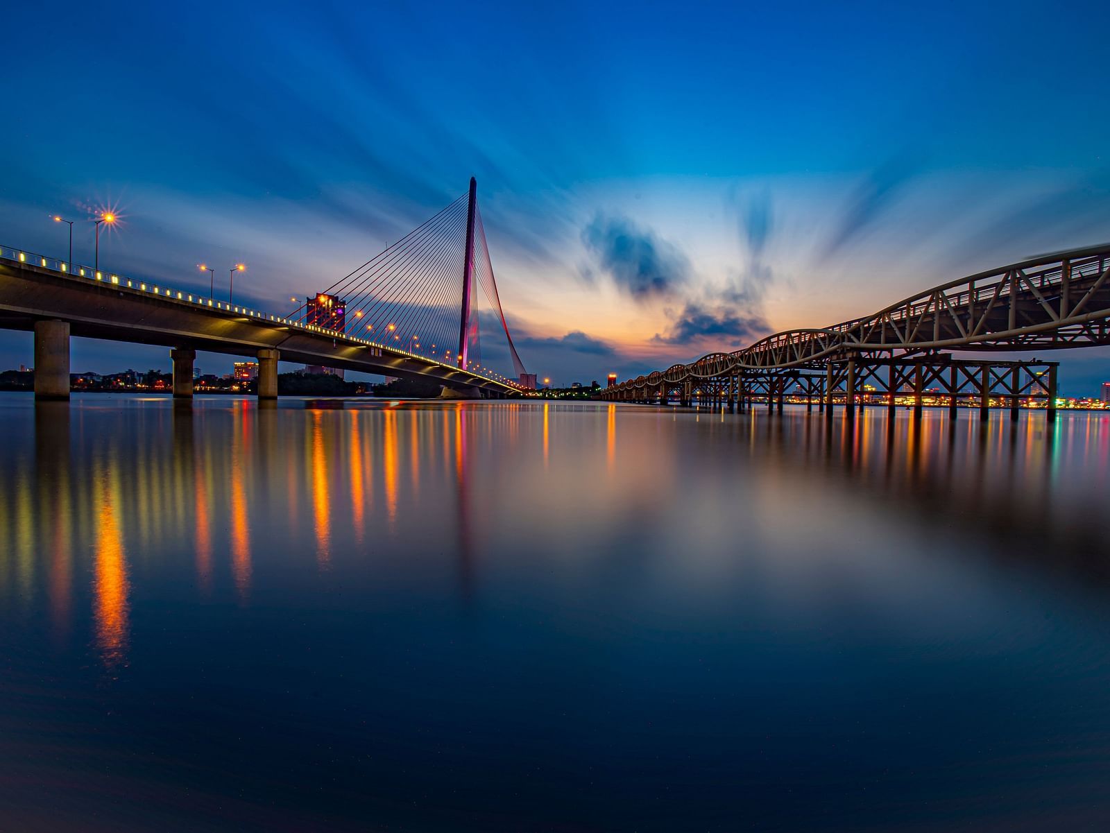 A view from the waterbody of two bridges with lights on during twilight in Vietnam.