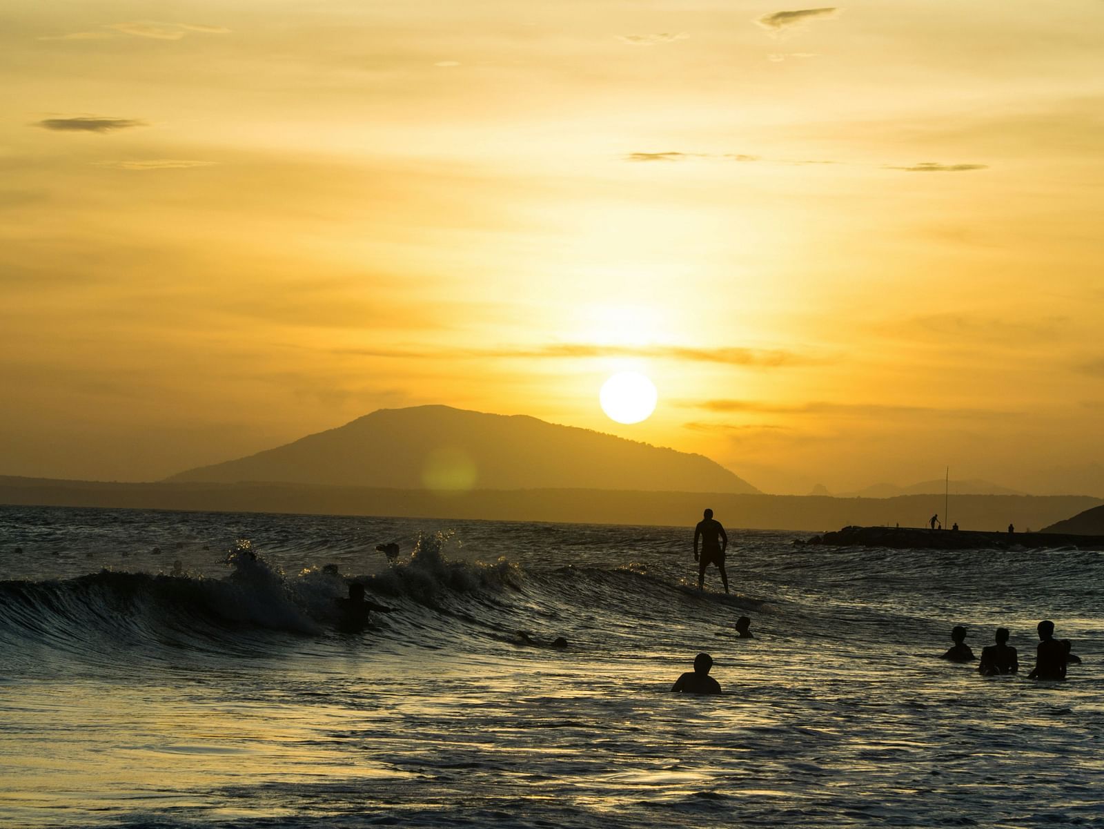 An overview of a beach in Mui Ne with people swimming and surfing, and the sun setting in the background.
