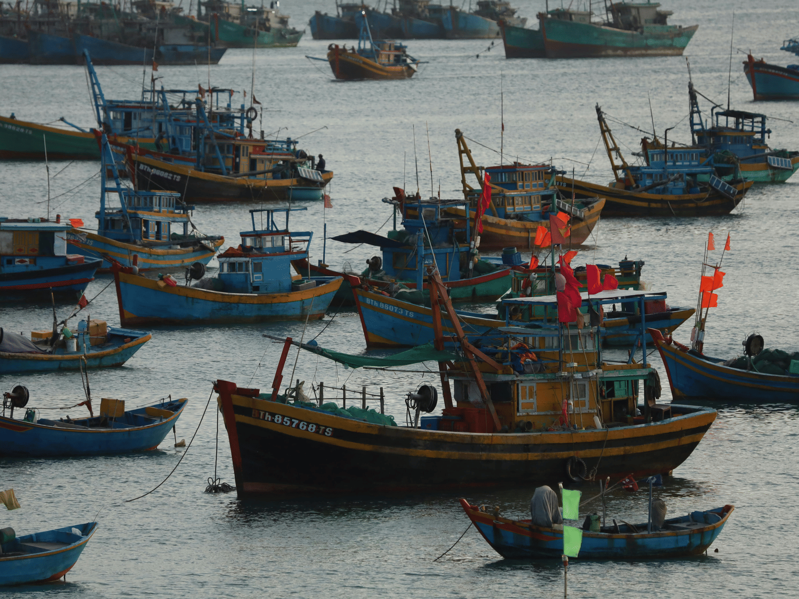 A cluster of many colourful, traditional wooden fishing boats anchored in a harbour on a cloudy day.