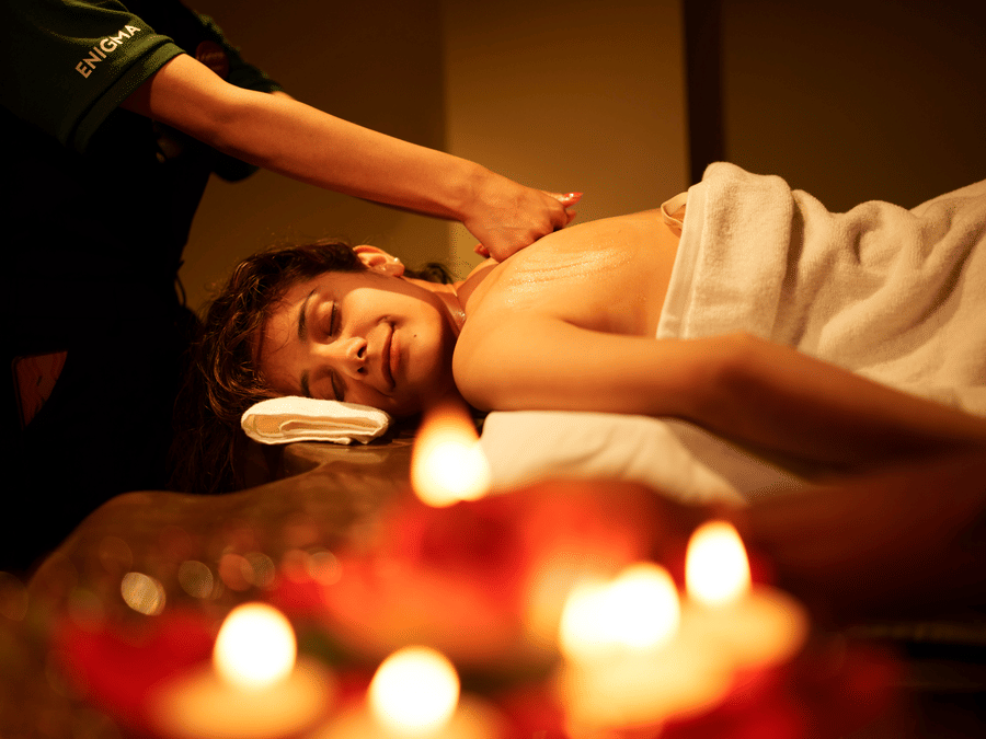 A person is receiving a massage with lit candles in the foreground, indicating a tranquil spa treatment area at Summit Enigma Resort and Spa