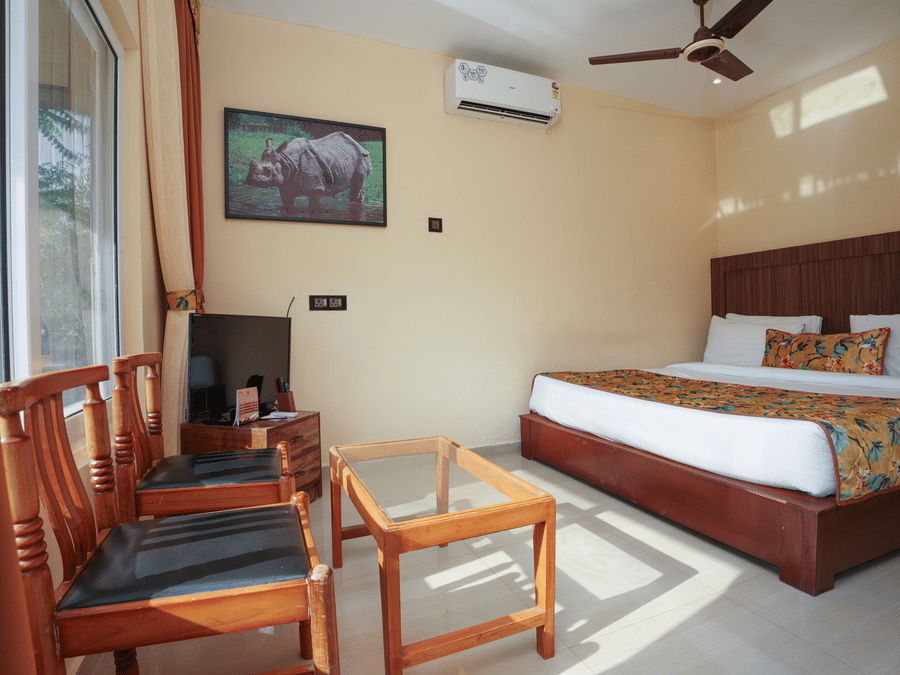 Deluxe Cottage featuring a spacious bed, television, air conditioner, glass table, and chairs at Summit Green Lake Tea Resort & Spa, Kaziranga