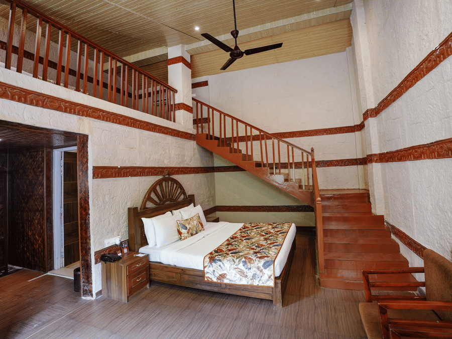 Duplex ethnic villa featuring a spacious bedroom and staircase leading to an additional room at Summit Green Lake Tea Resort & Spa, Kaziranga