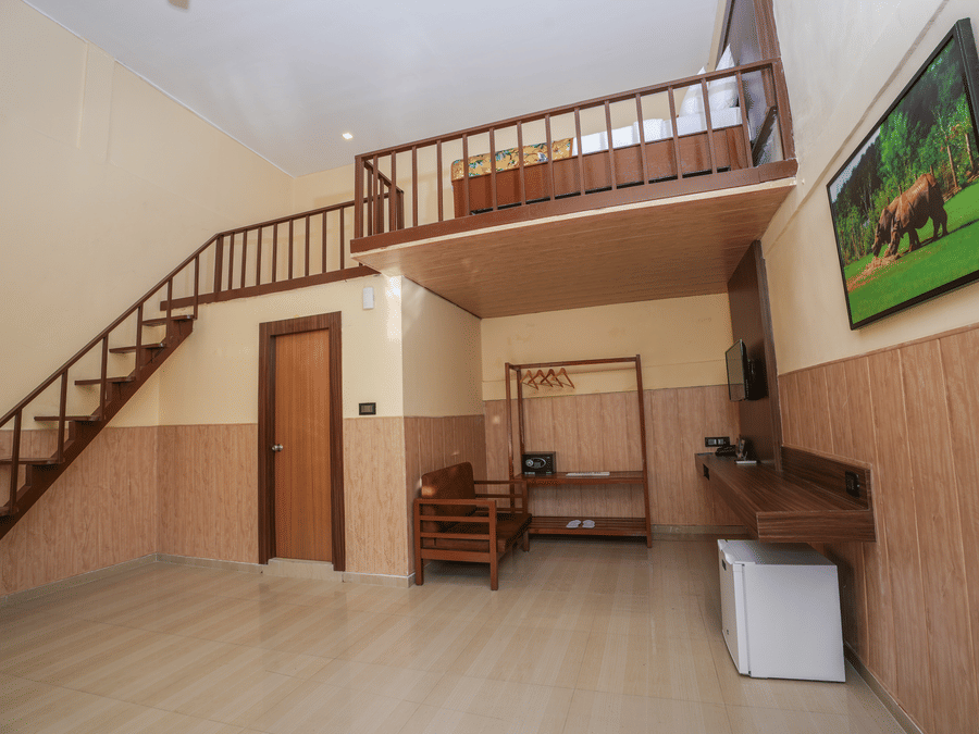 Duplex room with balcony features a living area with wooden furniture, a wine fridge, wall-mounted television, and stairs leading to the spacious bedroom at Summit Green Lake Tea Resort & Spa, Kaziranga