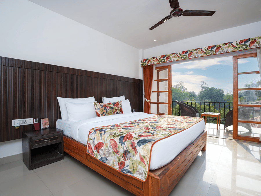 The suite with balcony offers a stunning nature view through large doors that open onto furniture and a glass table at Summit Green Lake Tea Resort & Spa, Kaziranga