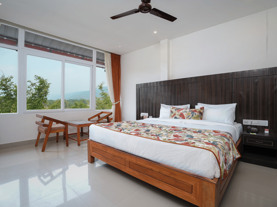 Deluxe room featuring large windows with a nature view, a spacious bed, air conditioning, wooden storage units, and a television at Summit Green Lake Tea Resort & Spa, Kaziranga4