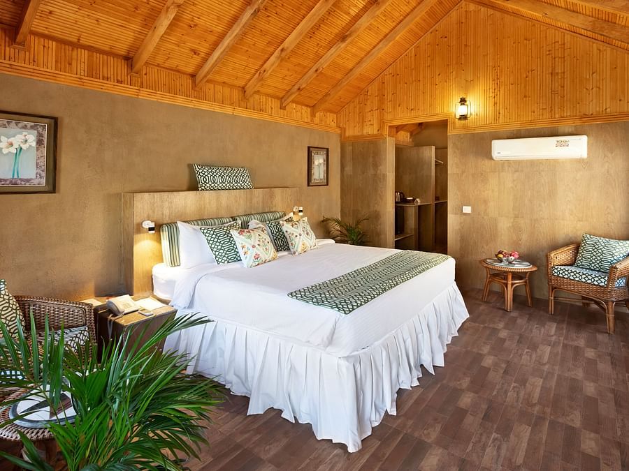 An image of an attic style bedroom featuring double size bed, a bedside table, flower pots, and a seating area at Suryavilas Luxury Resort & Spa, Kasauli