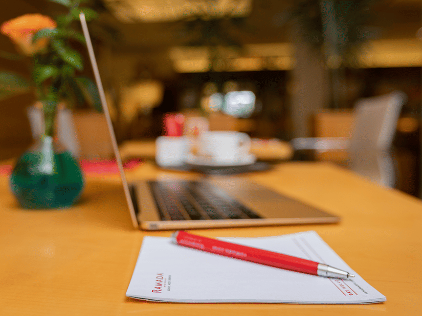 A laptop, notepad, and a flower vase kept on a table at Ramada by Wyndham Addis, featuring the best hotel offers at Ramada by Wyndham Addis, Addis Ababa