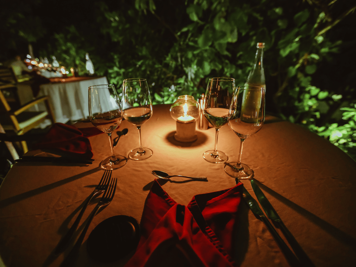 A wide-angle shot of dinning table setup outdoor with a brightly lit candle illuminating the entire table.