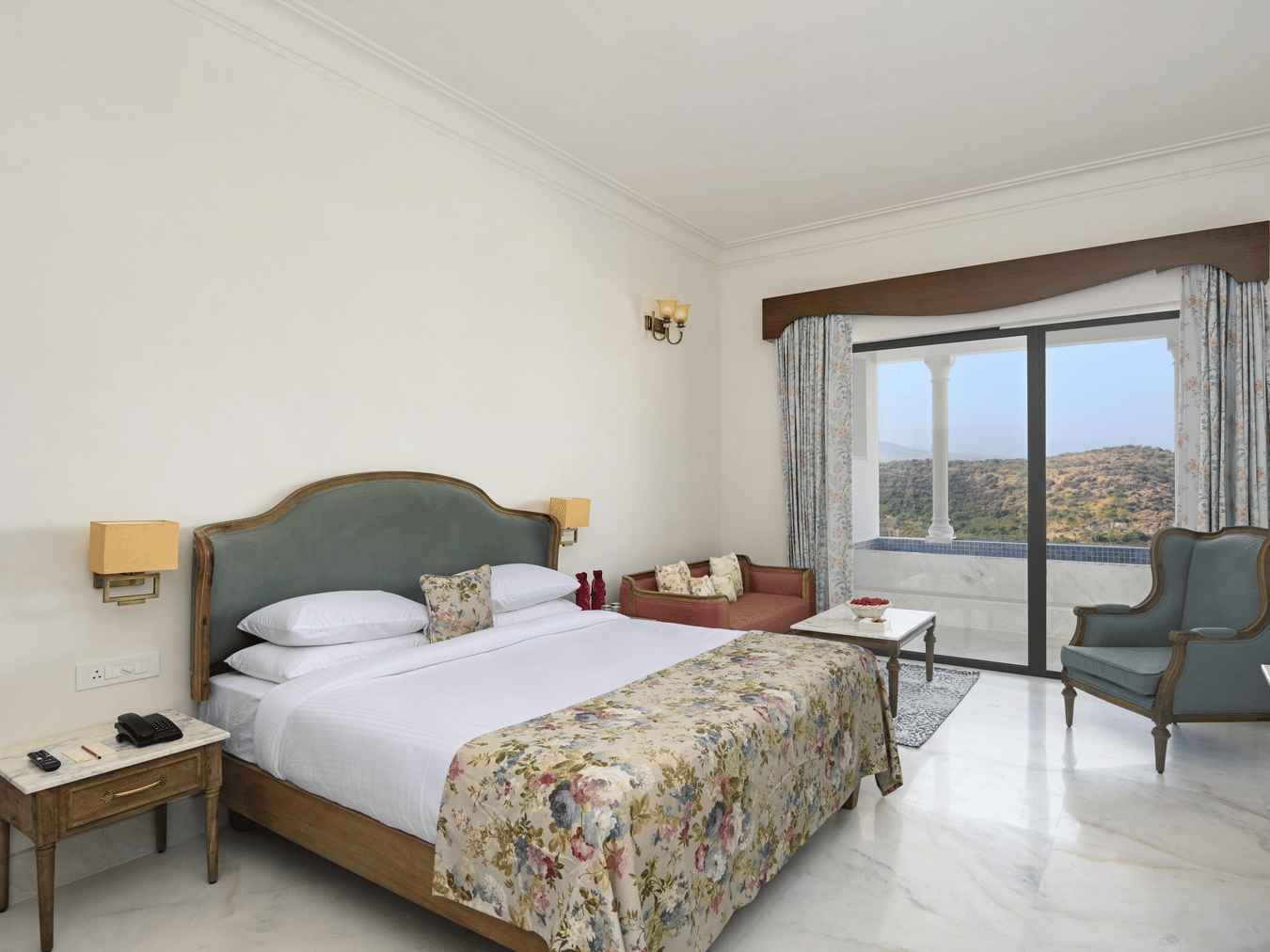 Interior view of the Plunge Pool Suite featuring a queen size bed, with side tables, lamps, a chair and a floor to ceiling sliding door to reach the plunge pool, offering the finest accommodation in Udaipur