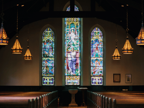 A church's interiors with stained glass and seats below the hanging lights