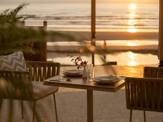 A close up shot of a table with two chairs at saz on the beach restaurant during sunset with sun rays reflecting on the sea waves in the background