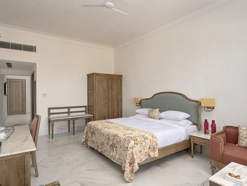 A room at Fateh Vilas, Udaipur, featuring a king size bed a wardrobe seating options and white ceiling fan