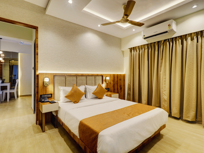 A bedroom featuring a plush bed with lamps on both sides and a doorway to the dining space of one of the best service apartments in Mumbai at Home2 Suites & Service Apartments