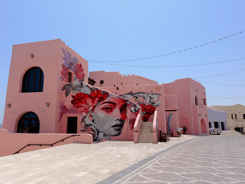 A vibrant mural featuring a woman's face and bright red flowers decorates the wall of a pink building.