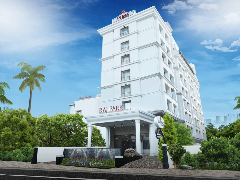 Facade view of Raj Park Hotel, Chennai, with trees on either side and blue sky in the background.