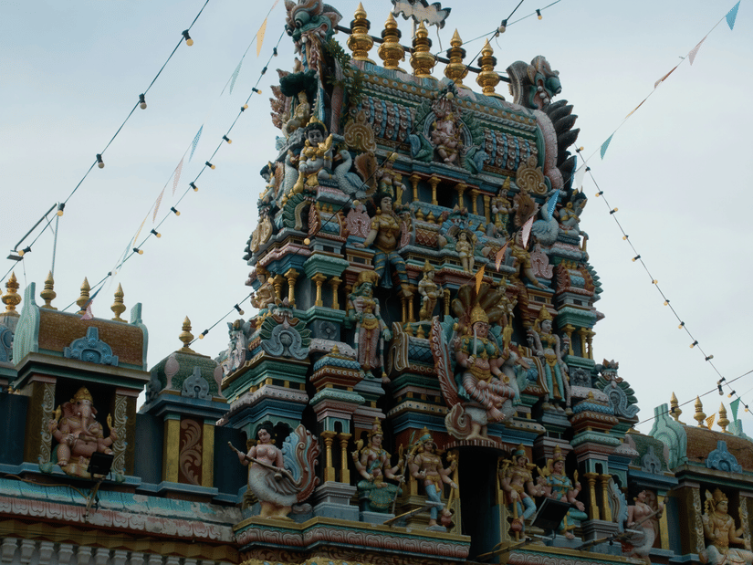 A view of a temple's facade with intricate art and miniature deities on the gopuram and blue sky in the background.