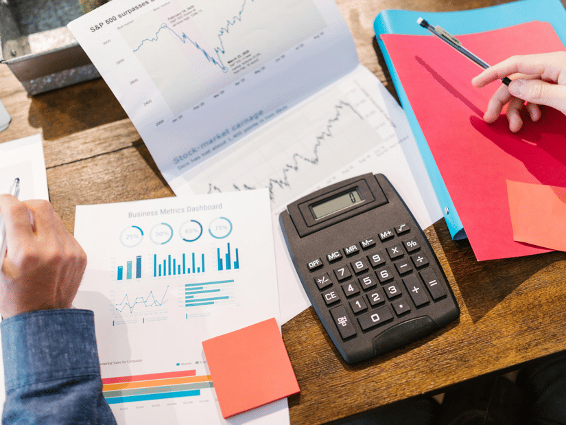 An overhead view of a desk showing hands working on documents, a calculator, and other office items.