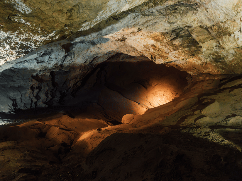 Interior view of an ancient rock-cut cave featuring natural stone formations and a softly illuminated chamber.