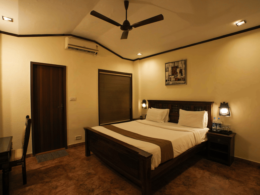 nterior view of a bedroom featuring a wooden bed, a work desk with a chair, side tables with lamps, and a ceiling fan.