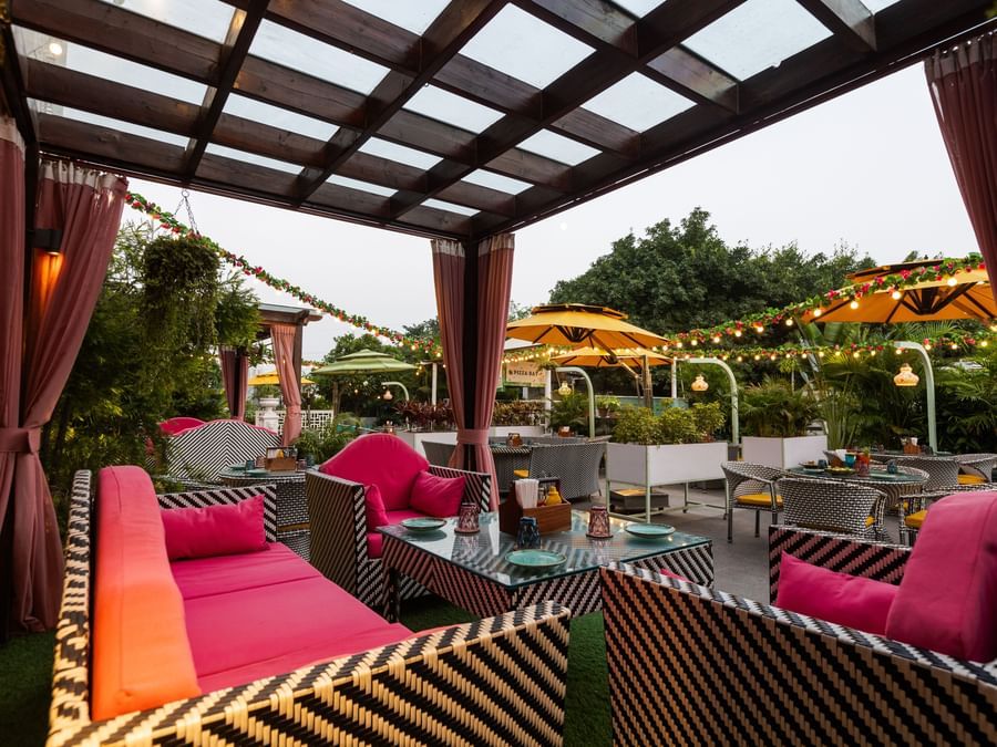A patio restaurant with outdoor seating featuring a zigzag pattern. A wooden pergola covers the area, which is lit by string lights and includes umbrellas and plants, creating a pleasant dining atmosphere - Karma Lakelands.