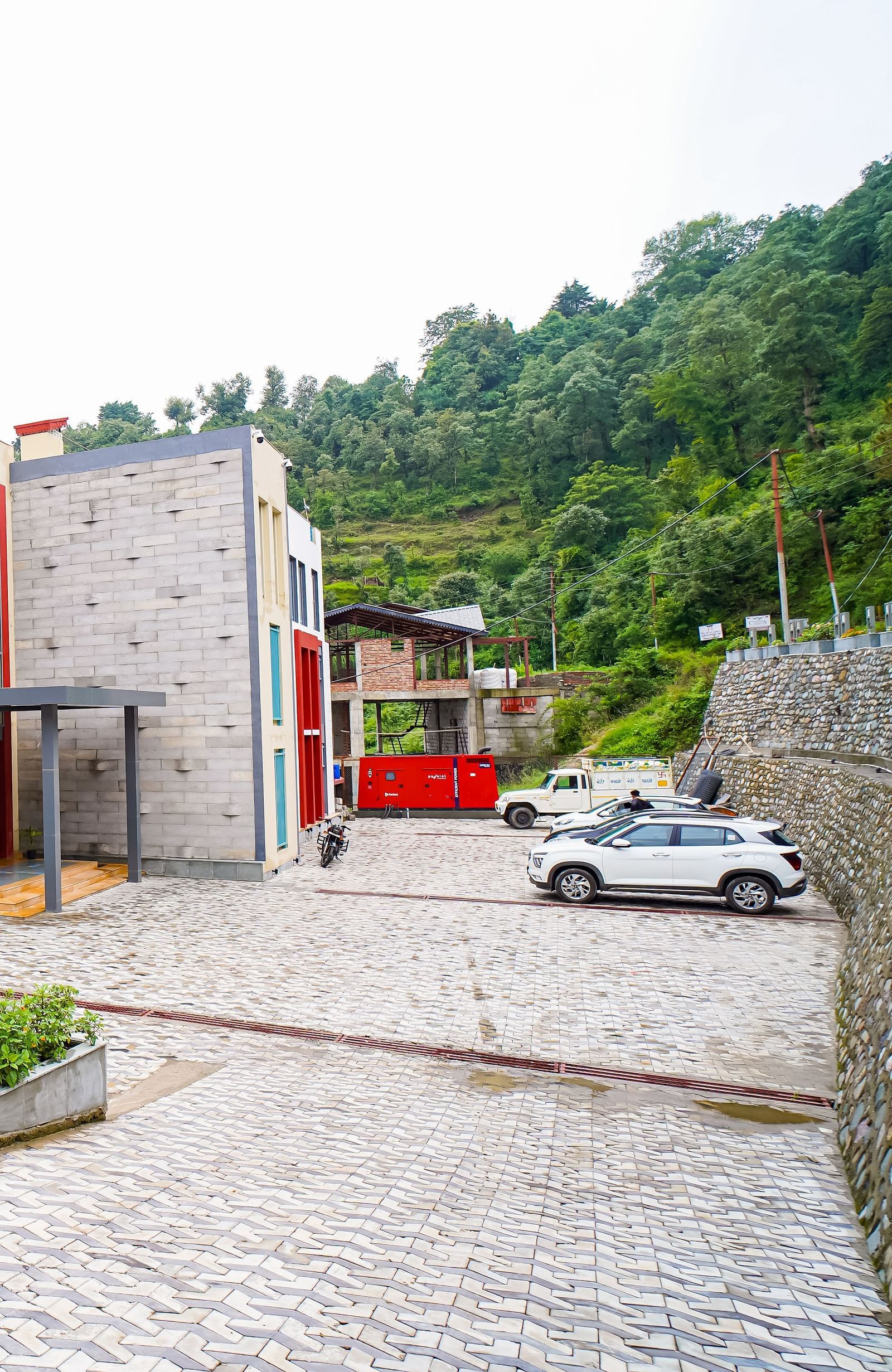 The exterior of a modern building with red and white sections and a paved courtyard is visible | Sukama Resort & Spa, Nainital