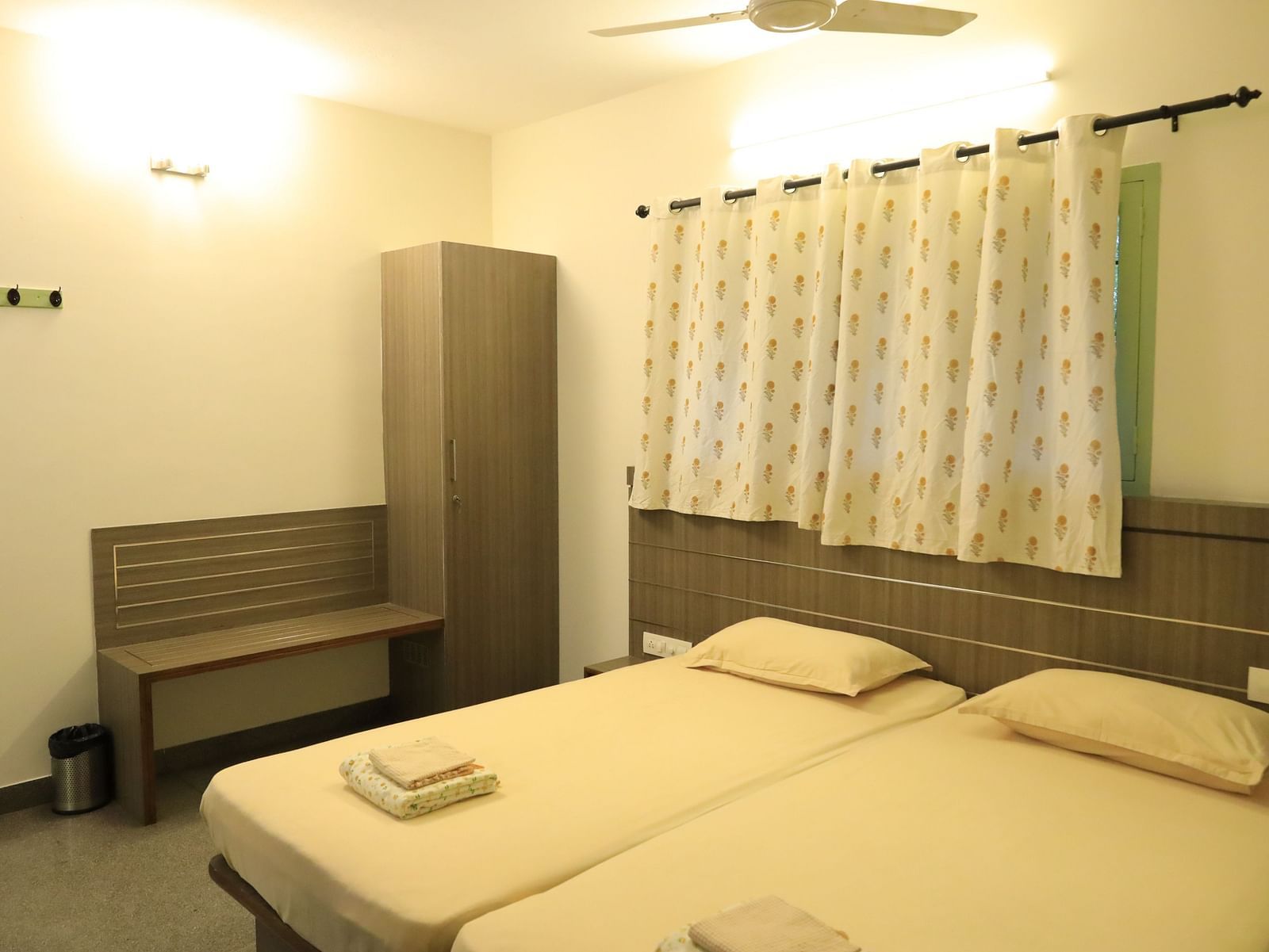 A bedroom at Wyt Hotels Transit Nest, Madurai featuring two single beds, bedside table, and a bench attached to it.