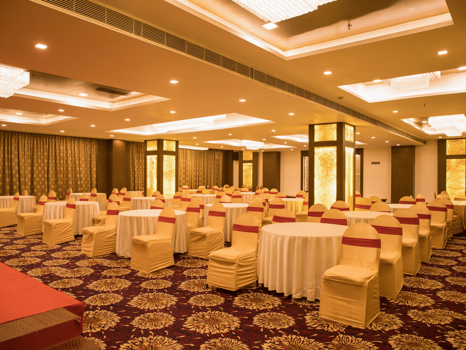 A spacious banquet hall at Benzz Park Chennai with numerous round tables draped in white, set for a gathering.