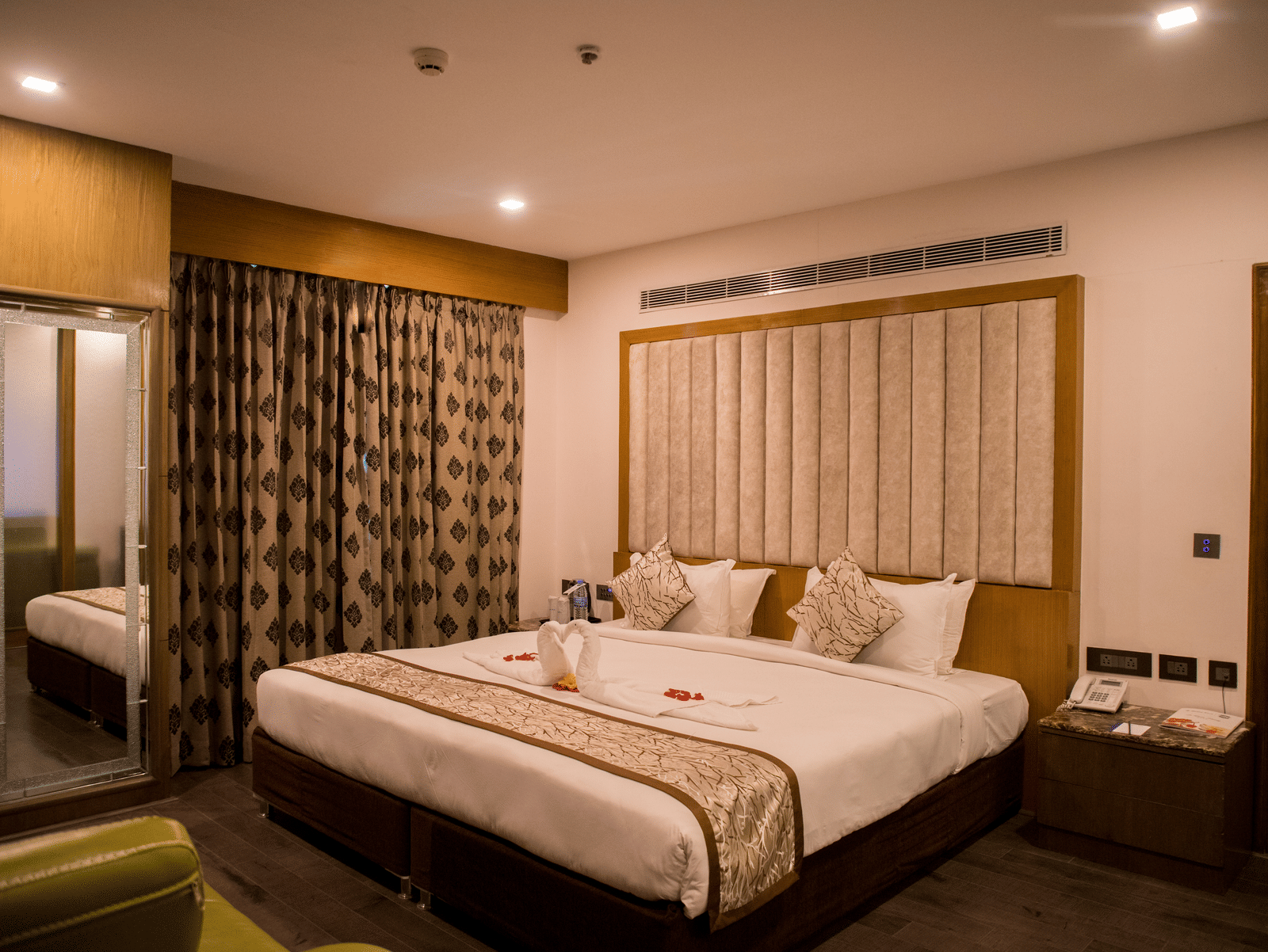 A hotel room at Benzz Park Chennai featuring a neatly made bed with white linens, a bedside table, and curtains.