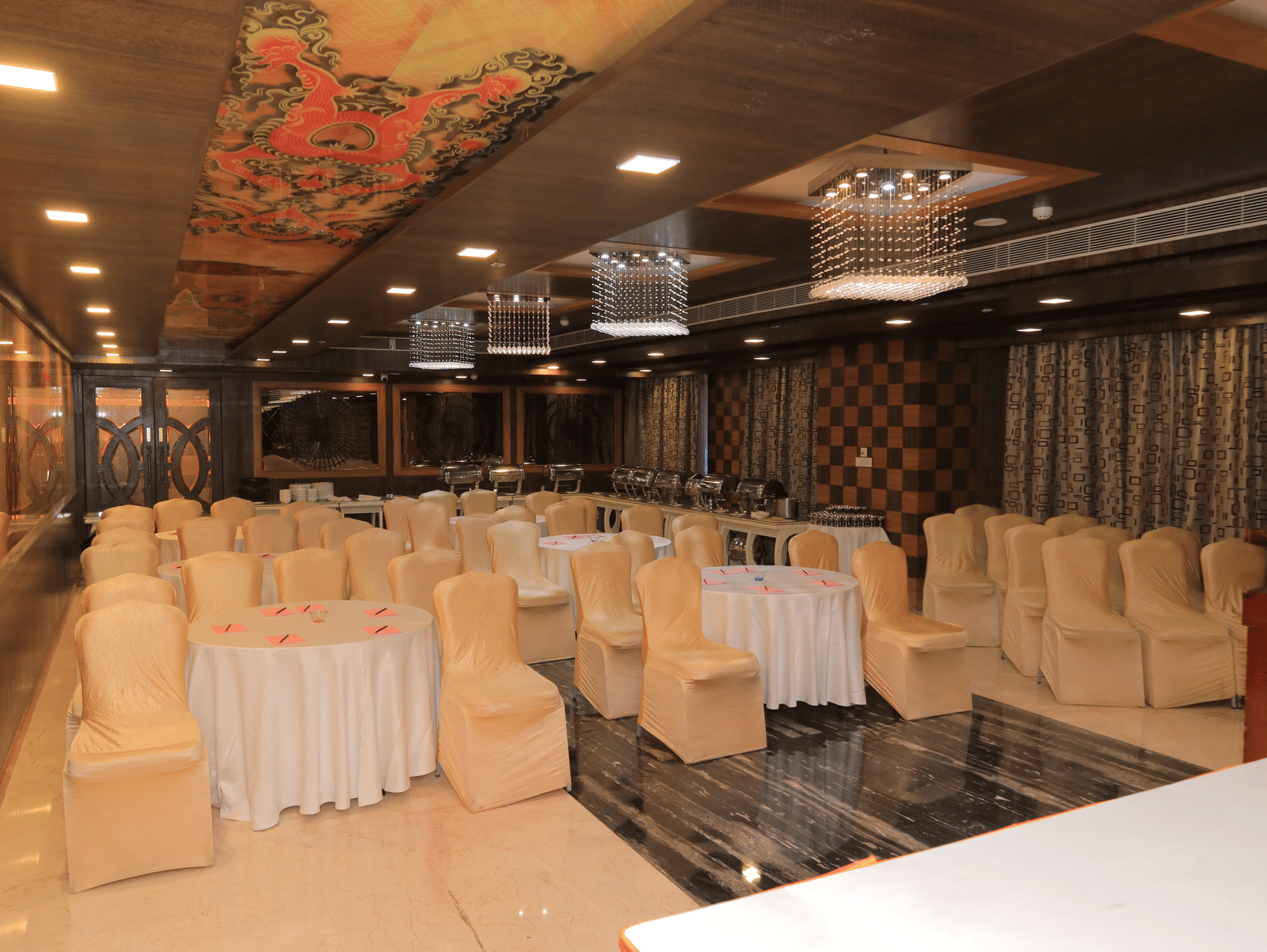 Corner view of the Bentley hall at Benzz Park, Vellore, featuring chairs surrounding round tables facing towards the stage in front of them.